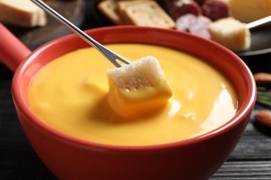 Dipping piece of bread into tasty cheese fondue at black table, closeup