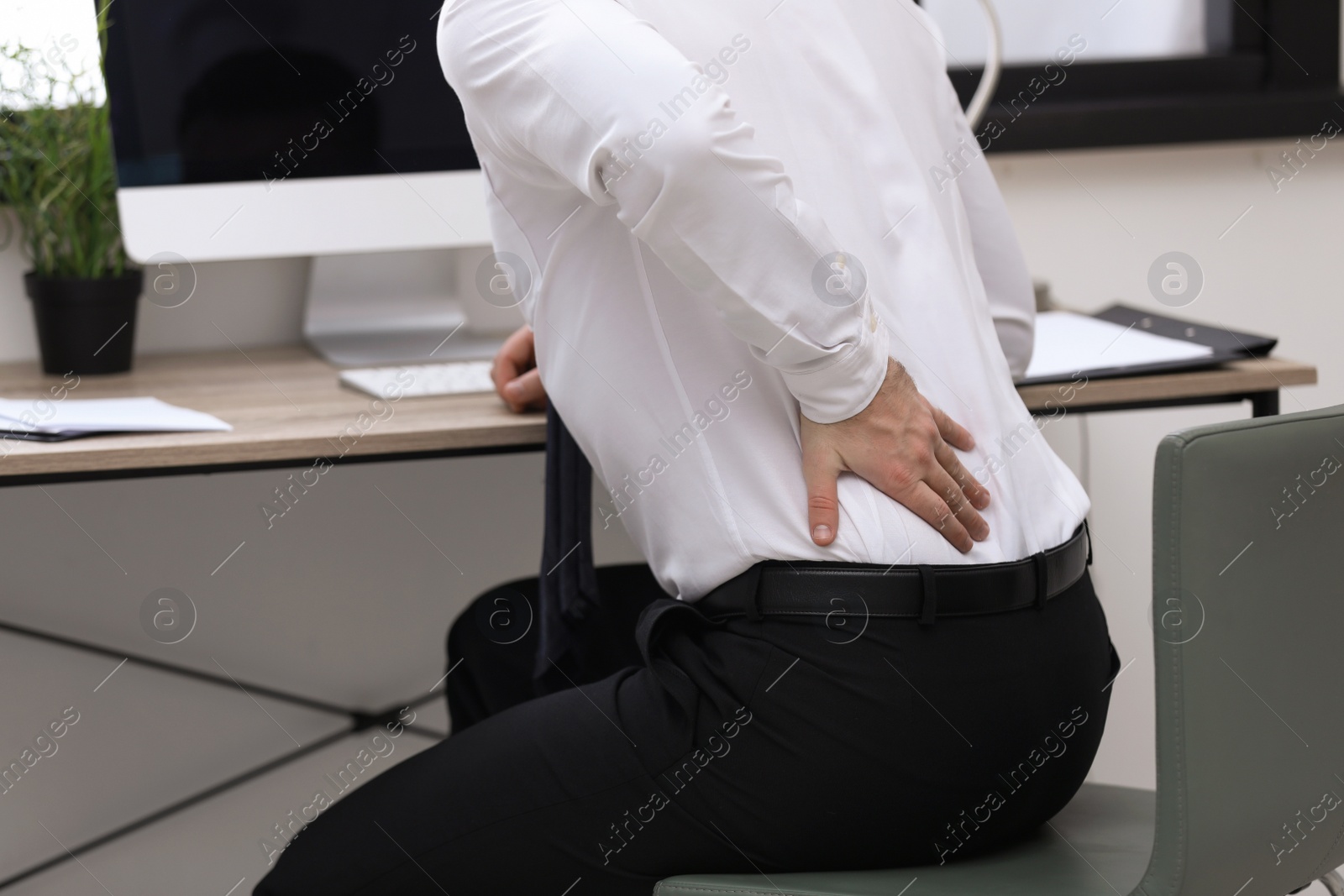 Photo of Businessman suffering from back pain at workplace, closeup