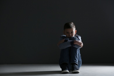 Photo of Upset boy sitting in dark room. Space for text