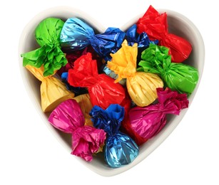 Photo of Heart shaped plate with candies in colorful wrappers isolated on white, top view