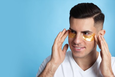 Man applying golden under eye patches on light blue background. Space for text