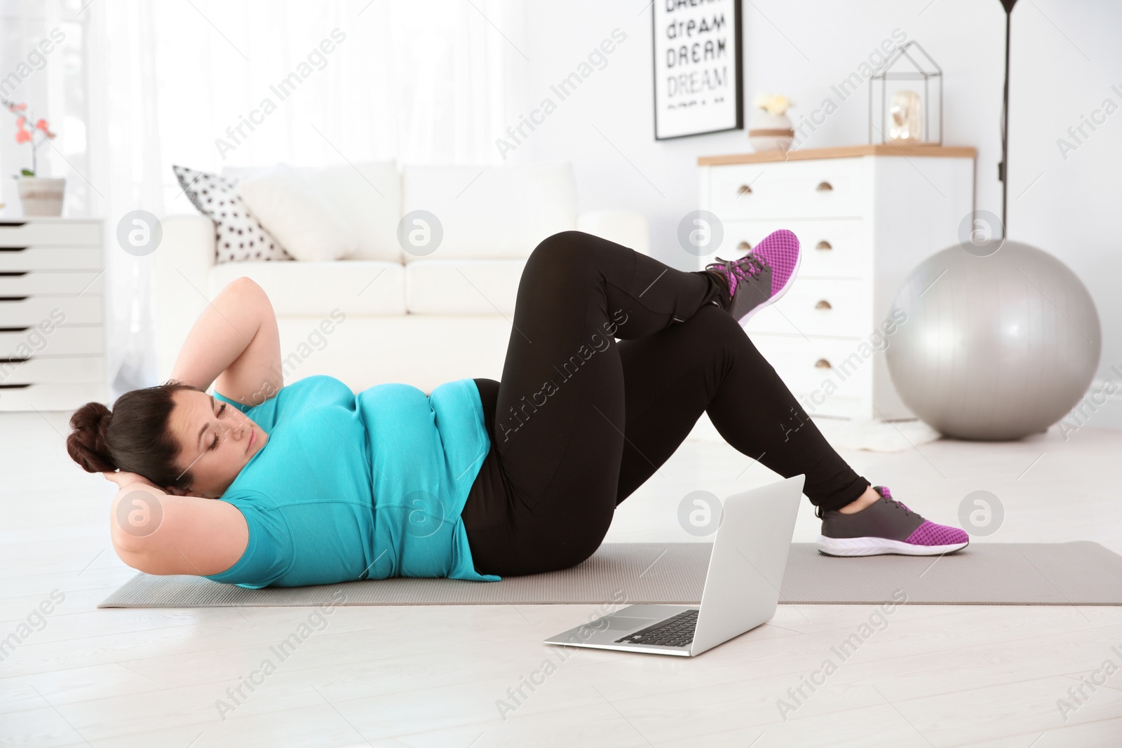 Photo of Overweight woman doing exercise while watching tutorial on laptop at home