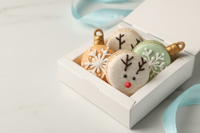 Photo of Beautifully decorated Christmas macarons in box and ribbon on white table, space for text