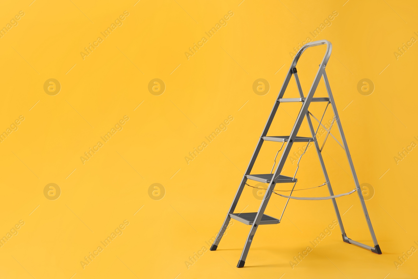 Photo of Modern metal stepladder on yellow background. Space for text