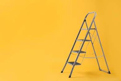 Modern metal stepladder on yellow background. Space for text