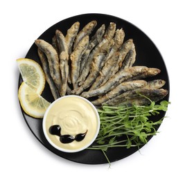 Plate with delicious fried anchovies, lemon slices, microgreens and sauce on white background, top view