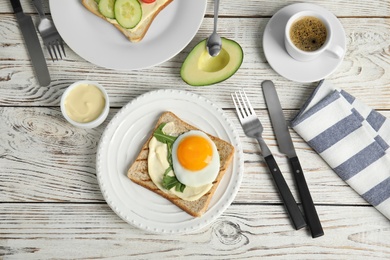 Slice of bread with fried egg, spread and arugula on white wooden table, flat lay