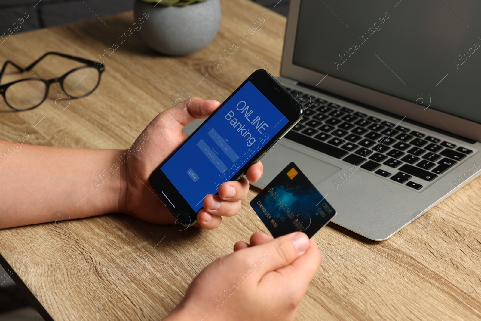 Photo of Man using online banking app on smartphone and credit card at wooden office table, closeup