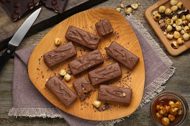 Delicious chocolate candy bars with caramel and nuts on wooden table, flat lay