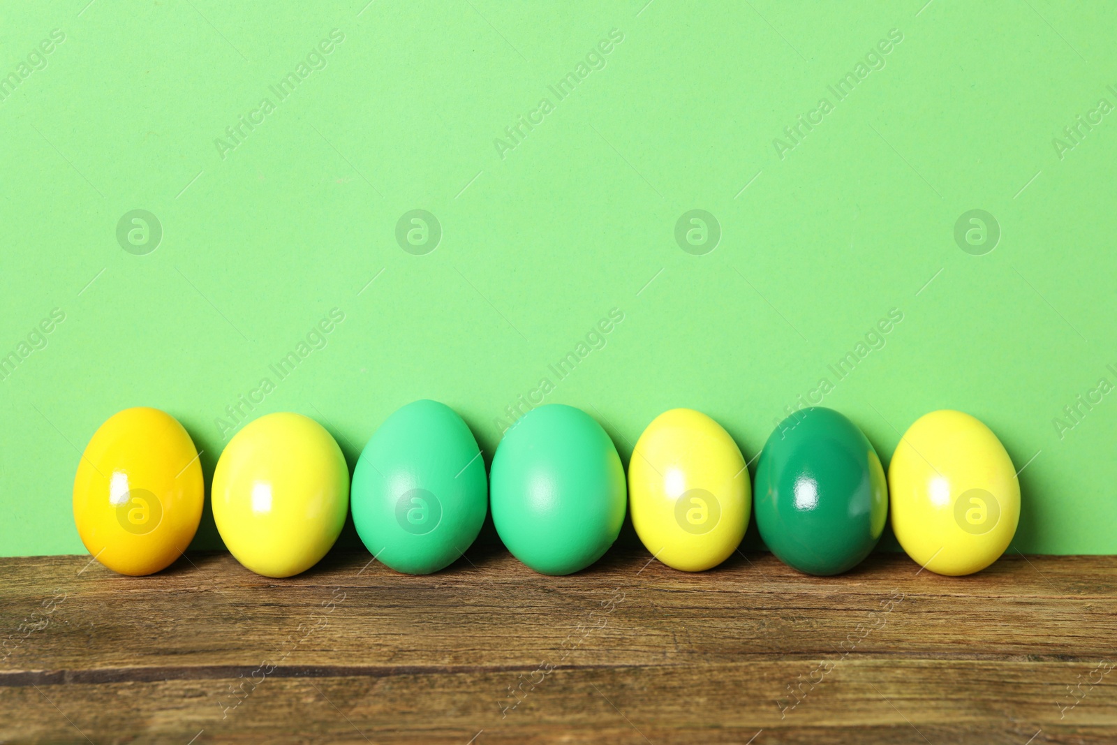 Photo of Easter eggs on wooden table against green background, space for text