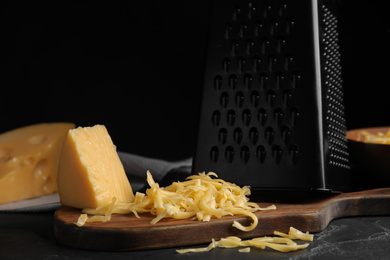 Photo of Delicious grated cheese on wooden board against black background