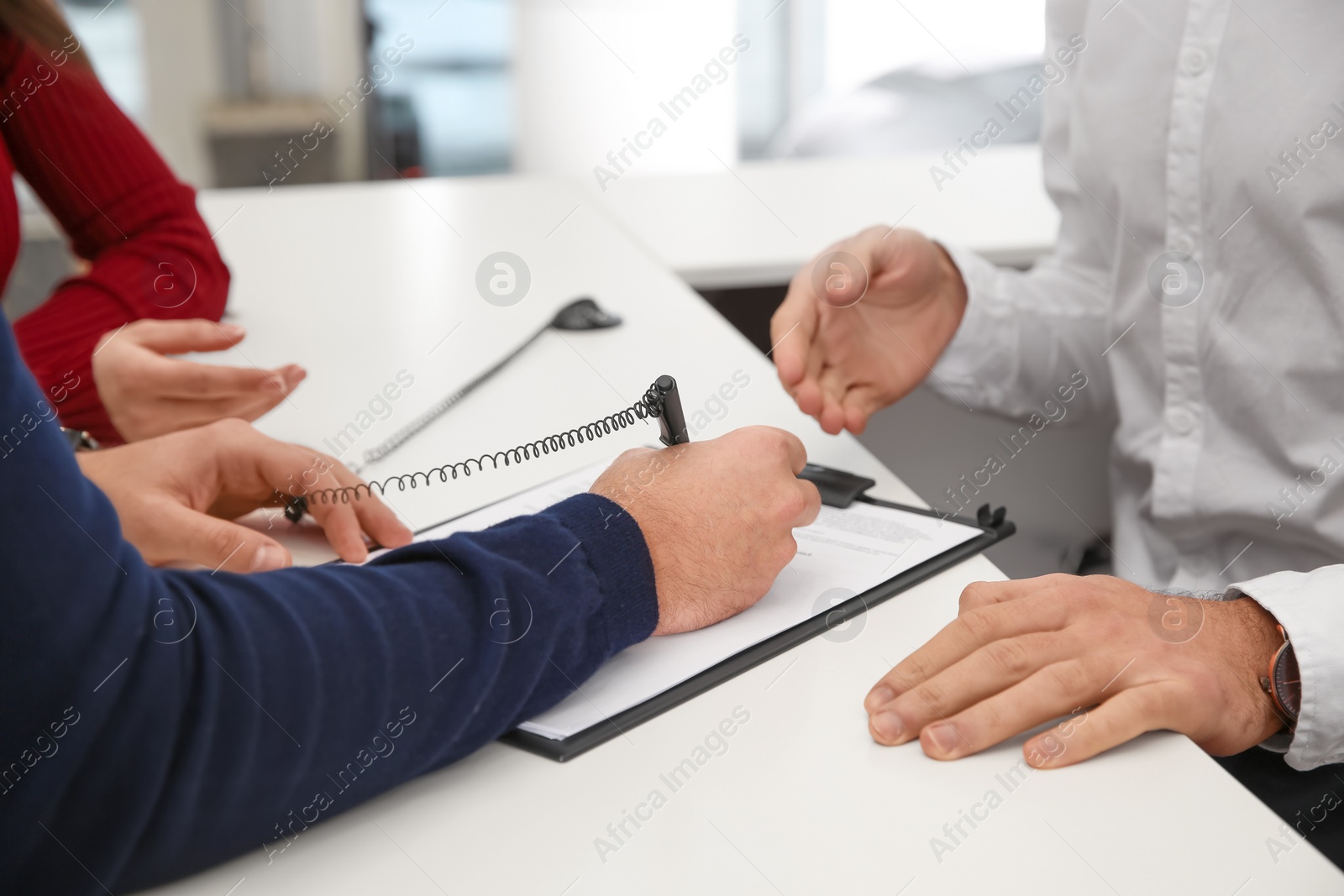 Photo of Man signing document at salesman's counter in car dealership, closeup