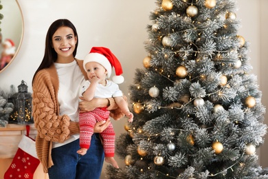 Photo of Mother with her cute baby near Christmas tree at home