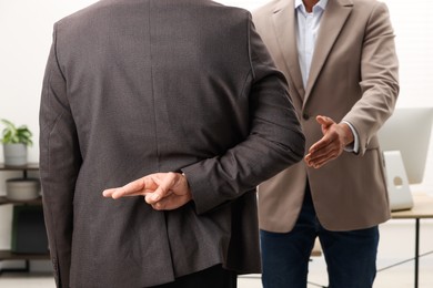 Photo of Employee crossing fingers behind his back while meeting with boss in office, closeup