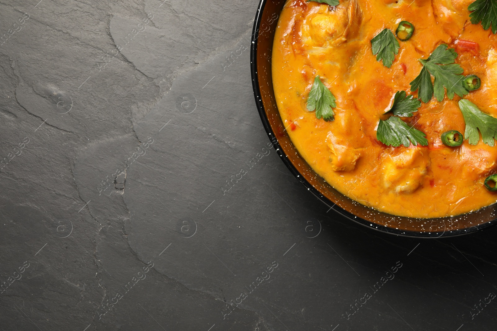 Photo of Tasty chicken curry with parsley and pepper on black textured table, top view. Space for text