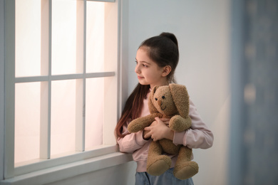 Photo of Cute little girl with toy near window at home