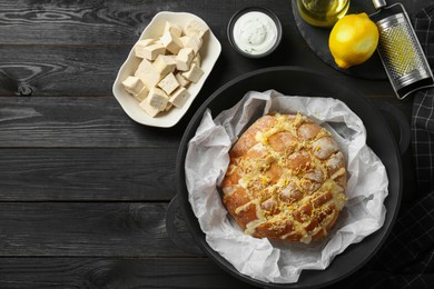 Photo of Freshly baked bread with tofu cheese and lemon zest served on black wooden table, flat lay. Space for text