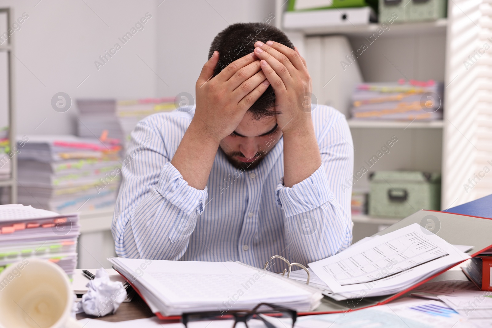 Photo of Overwhelmed man surrounded by documents at workplace in office