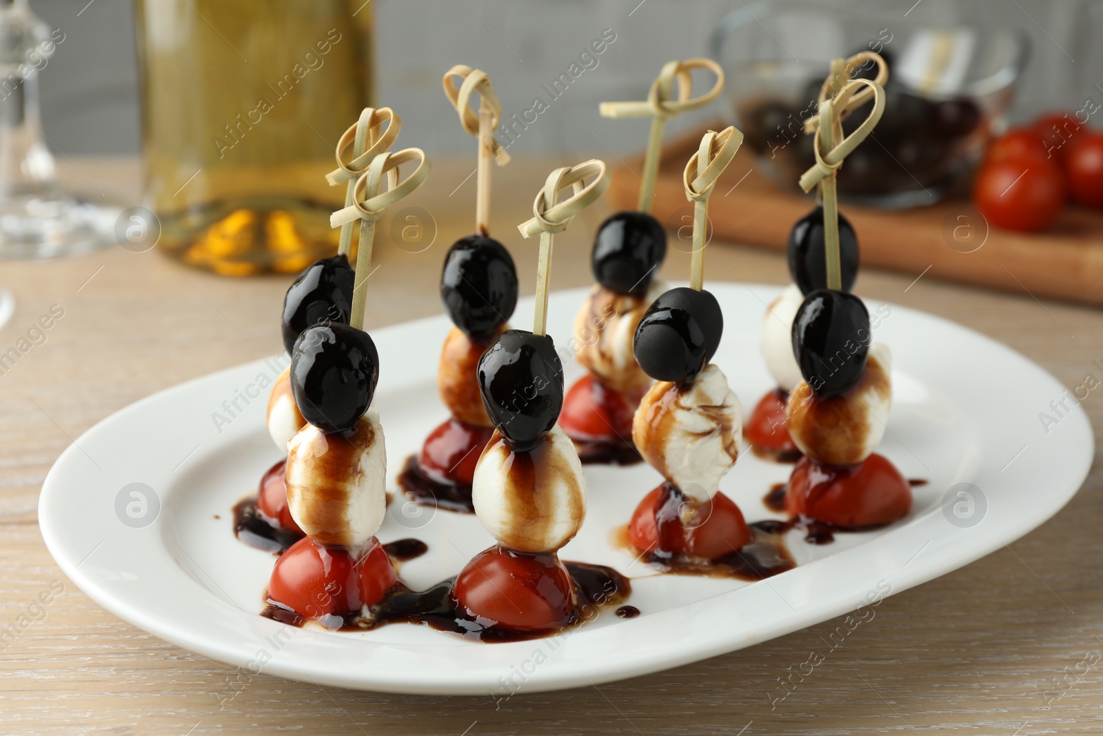 Photo of Tasty canapes with black olives, mozzarella and cherry tomatoes on light wooden table, closeup