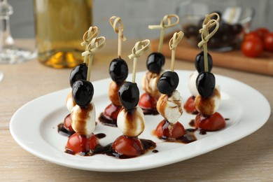 Tasty canapes with black olives, mozzarella and cherry tomatoes on light wooden table, closeup