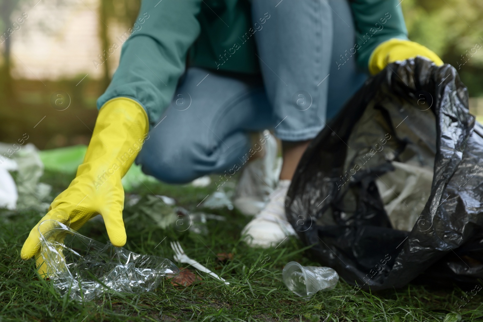 Photo of Woman with plastic bag collecting garbage in park, closeup