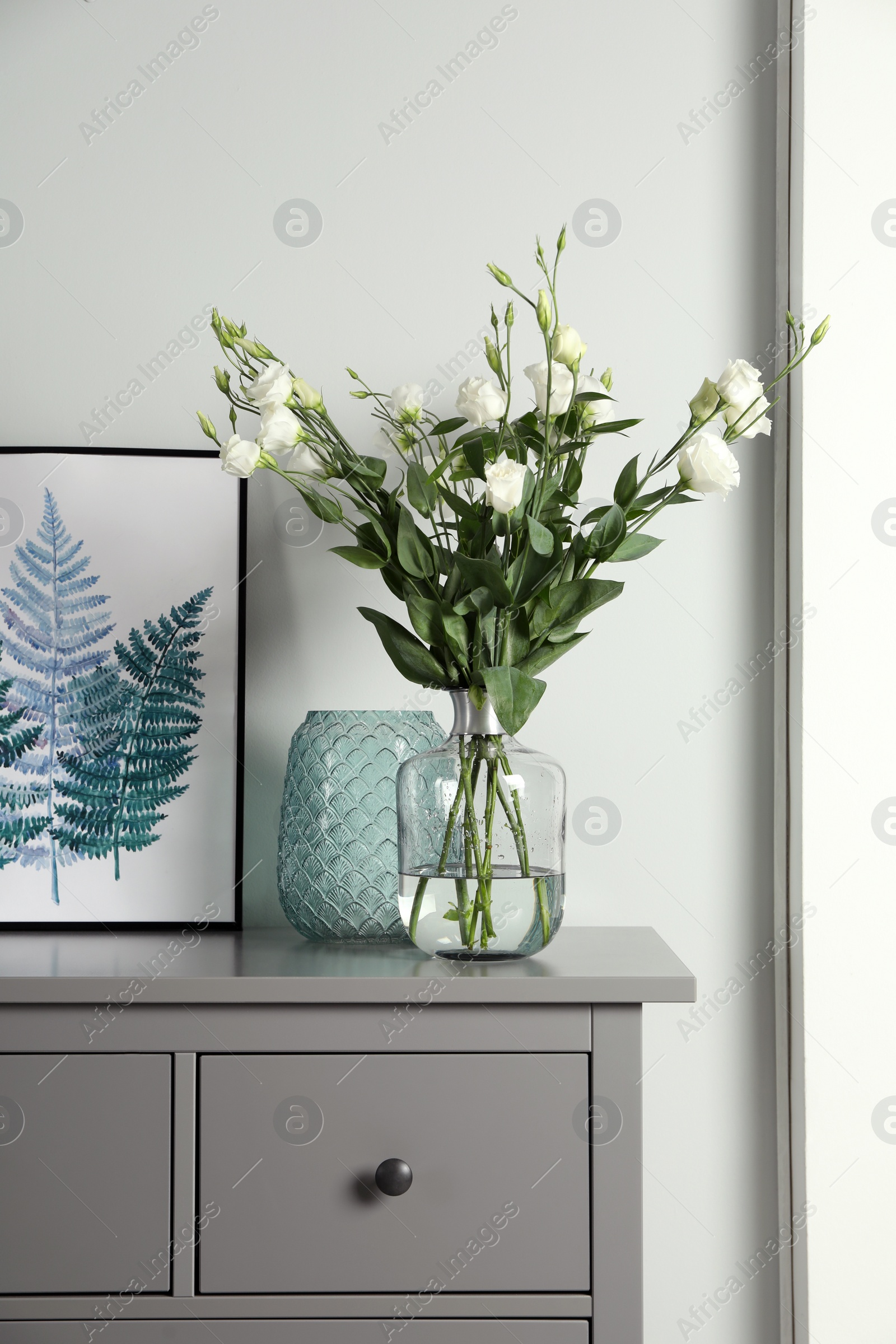 Photo of Composition with eustoma flowers in glass vase on grey cabinet indoors