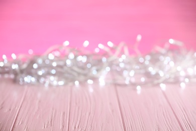 Photo of White Christmas lights on pink wooden table, blurred view