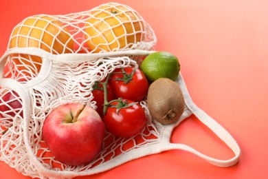 Photo of String bag with different vegetables and fruits on red background, closeup