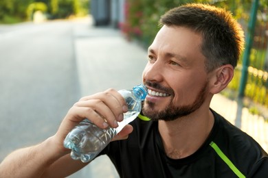 Photo of Happy man drinking water outdoors on hot summer day. Refreshing drink