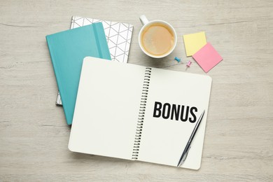 Image of Word Bonus written in notebook, coffee and stationery on wooden table, flat lay