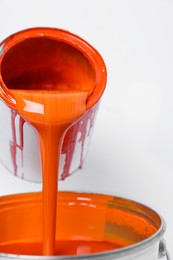 Photo of Pouring orange paint from can on white background