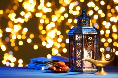Arabic lantern, Quran, dates and Aladdin magic lamp on table against blurred lights at night. Space for text