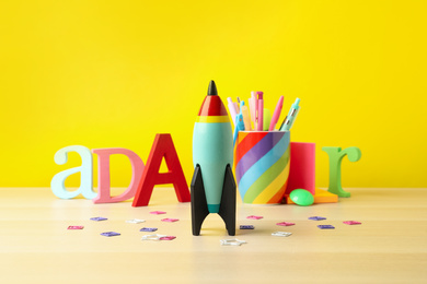 Bright toy rocket and school supplies on wooden table