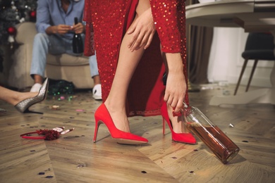 Photo of Woman with bottle of alcohol in messy room after New Year party, closeup of legs