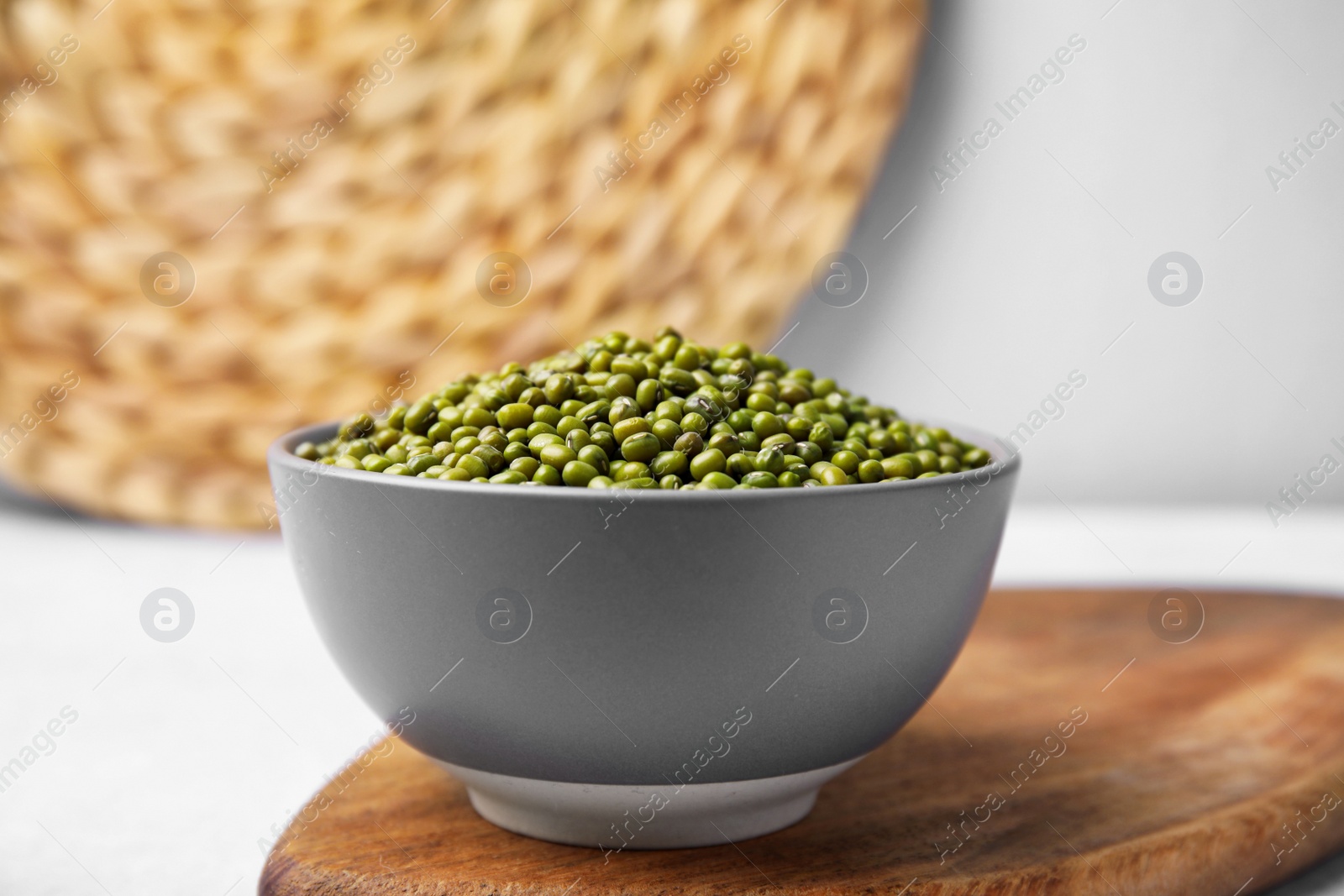 Photo of Bowl with green mung beans and wooden board on white table, closeup