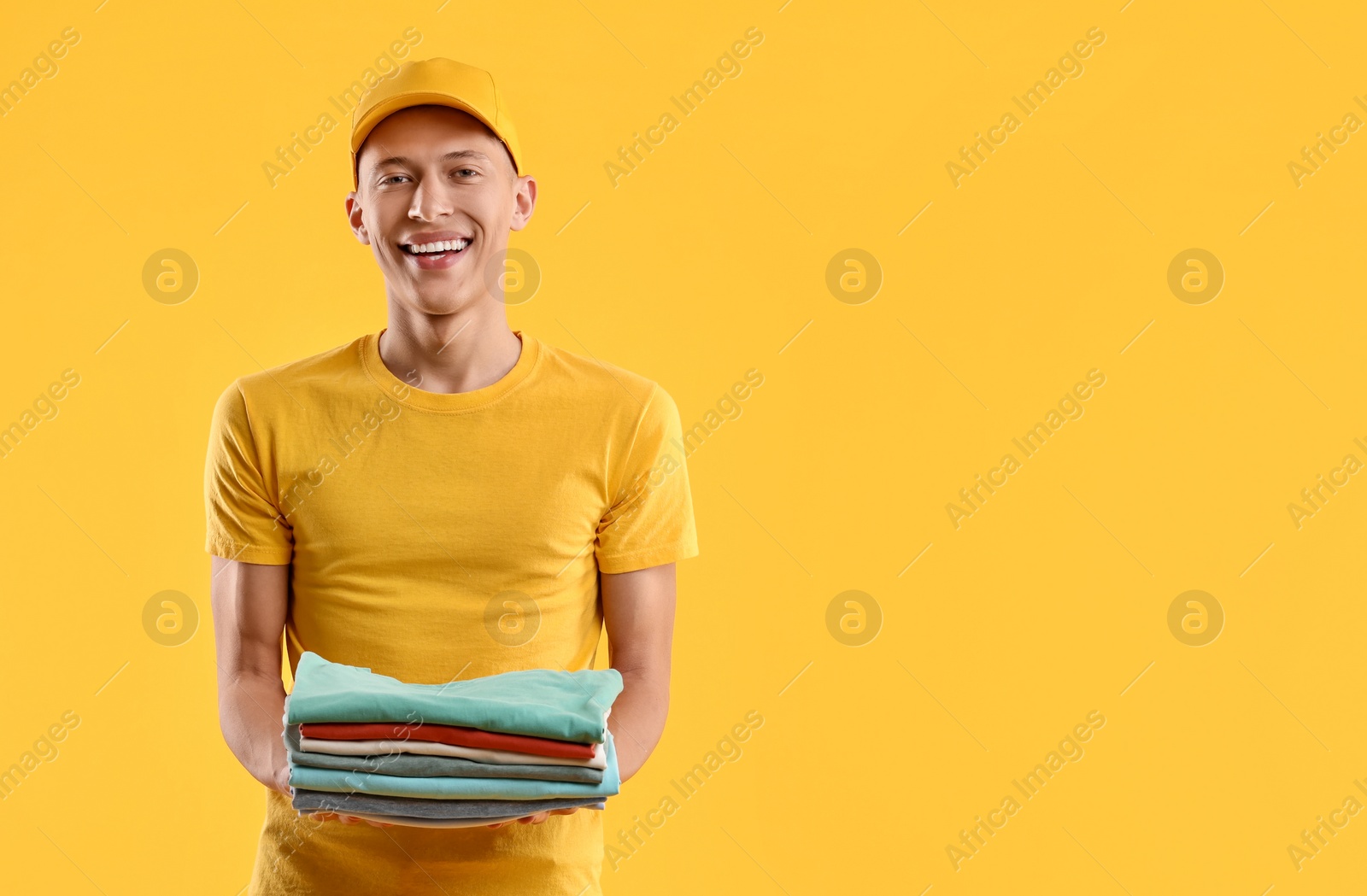 Photo of Dry-cleaning delivery. Happy courier holding folded clothes on orange background, space for text