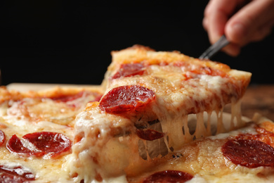 Photo of Woman taking slice of tasty pepperoni pizza at table, closeup