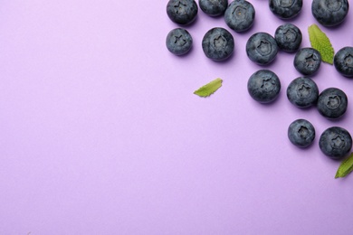 Photo of Tasty ripe blueberries and leaves on violet background, flat lay with space for text