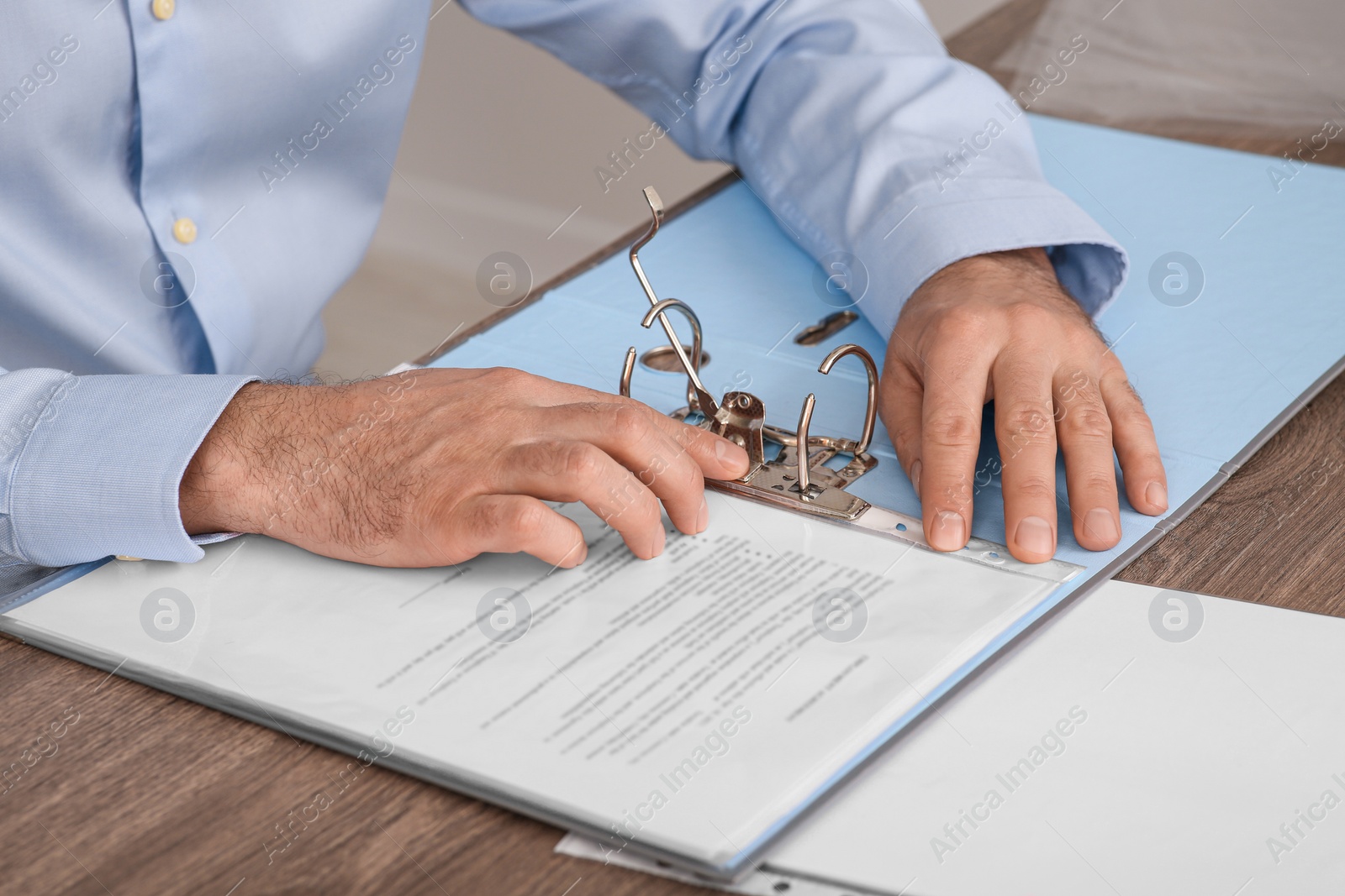 Photo of Businessman putting document into file folder at wooden table in office, closeup