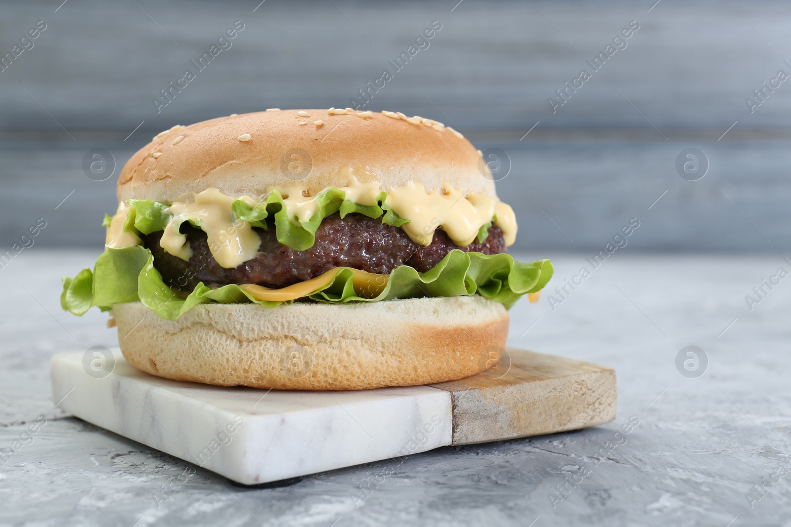 Photo of Delicious cheeseburger on grey textured table, closeup. Space for text