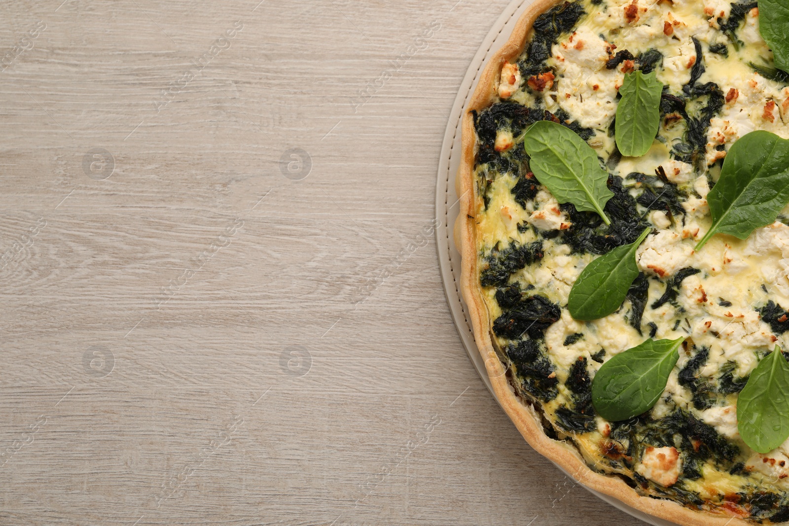 Photo of Delicious homemade spinach quiche on wooden table, top view. Space for text