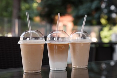 Photo of Plastic takeaway cups of delicious iced coffee on table in outdoor cafe