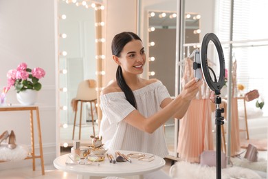 Photo of Beauty blogger preparing for video recording in dressing room at home. Using ring lamp and smartphone