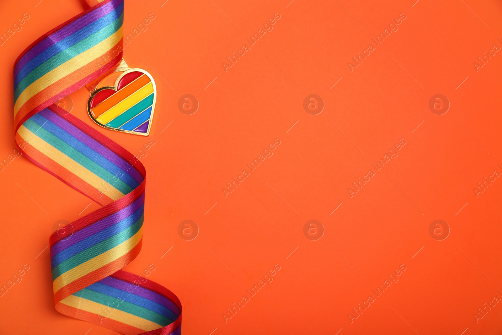 Photo of Rainbow ribbon with heart shaped pendant on orange background, top view and space for text. LGBT pride