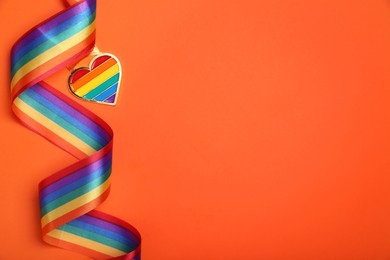Photo of Rainbow ribbon with heart shaped pendant on orange background, top view and space for text. LGBT pride