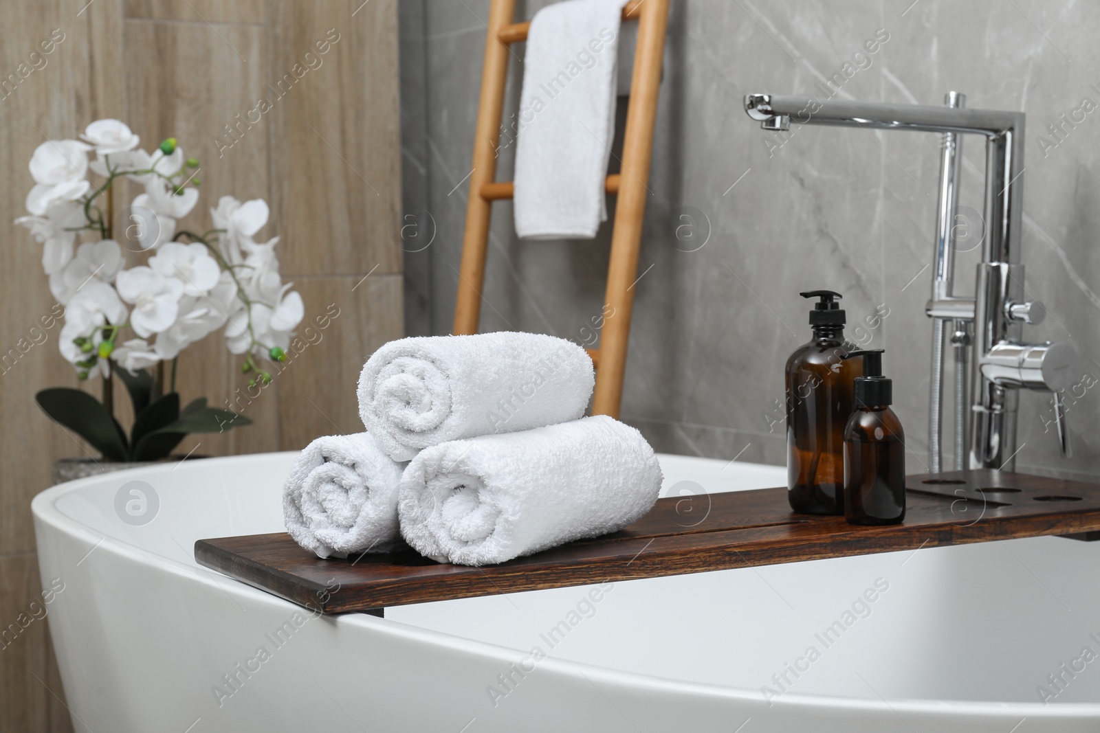 Photo of Rolled towels and personal care products on tub tray in bathroom