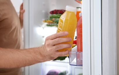 Photo of Man taking bottle with juice out of refrigerator in kitchen, closeup