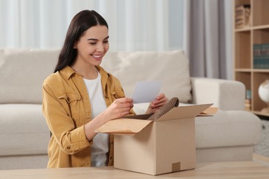 Happy woman holding greeting card near parcel with Christmas gift at home