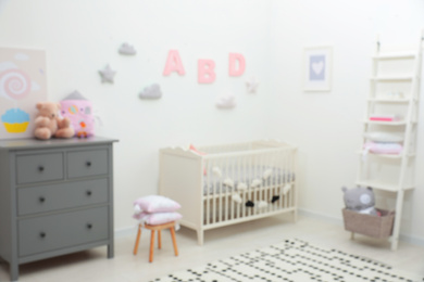 Photo of Blurred view of cute baby room interior with modern crib near white wall