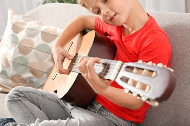Cute little boy playing guitar on sofa in room